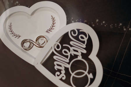Gold wedding rings lie in a wooden box in the shape of a heartの写真素材