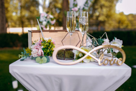 Outdoor wedding ceremony, decorated with a table with fresh flowers, glasses of champagne, an infinity sign and a glass box under the ringsの写真素材