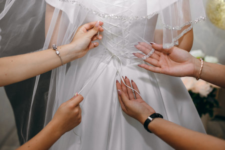 Wedding morning. Bridesmaids helping to put on wedding white dress, hands close up