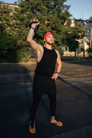 Man athlete lifts a kettlebell, training outdoors at sunsetの写真素材