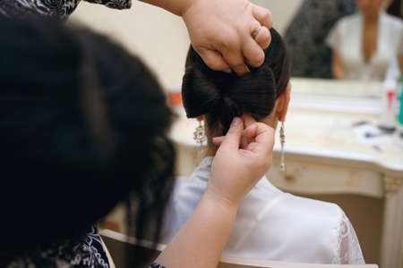 A professional hairdresser makes a beautiful slender brunette brides hair by braiding a hair bow.の写真素材