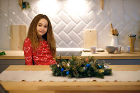 Happy baby girl sitting at the table in the home kitchen. The girl is dressed in red Christmas pajamas.の写真素材