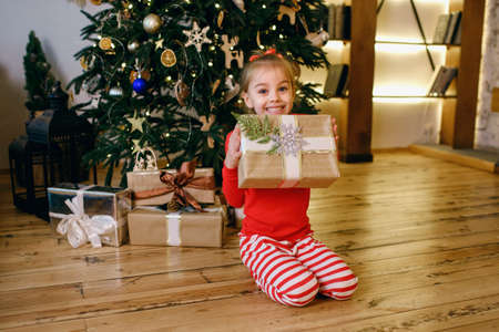A little girl near a decorated Christmas tree is holding a Christmas present. Christmas and New Year holidays concept.の写真素材