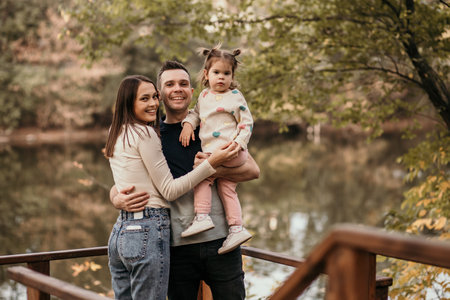 Happy dad, mom and their little daughter are walking by the river in the parkの写真素材