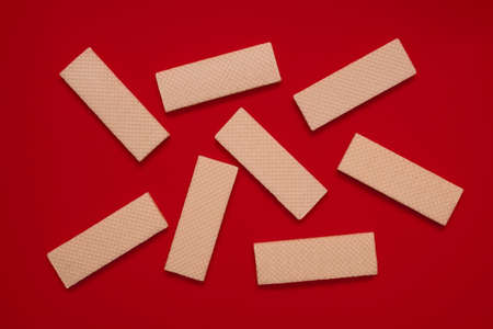 Chaotically scattered waffle cookies on a red background top view. Delicious pastries for coffee or tea. An excellent sweet dessert loved by children and adults. Pastry background rectangular shapeの写真素材