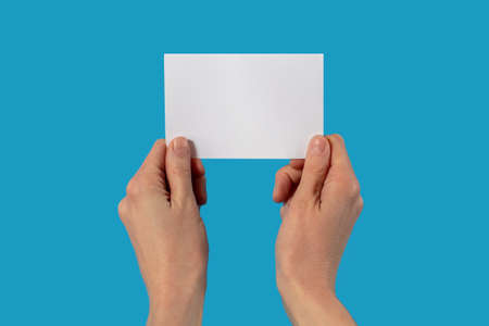 A man two hands holds a blank sheet of paper on a blue background with empty space for text