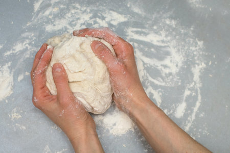 A woman in the kitchen kneads dough on a gray table at home