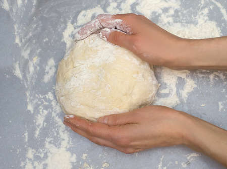 A woman in the kitchen kneads dough on a gray table at home. A man kneads the dough for baking with...