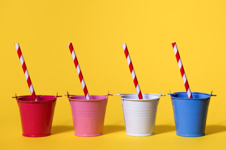 Four buckets on a yellow background with striped red and white straws