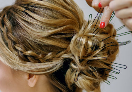 Professional stylist with red manicure doing hairdo in the womens beauty salon