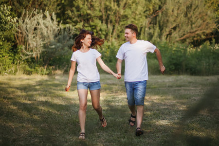 A young couple in love runs along the lawn and holds each others hands, smiling and having funの写真素材
