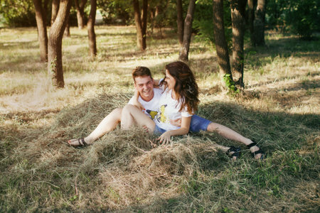 A young couple in love is lying on the mown grass. A man and a woman have fun and indulge in hay throwing each otherの写真素材