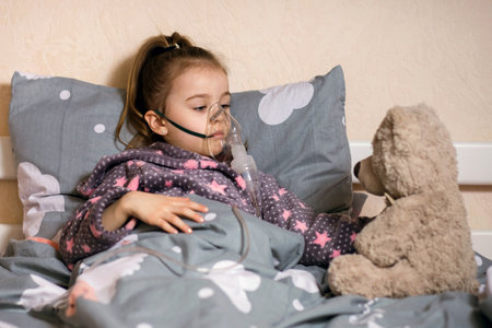 A little cute girl is sick and is treating a severe cough or allergy at home with an inhalerの写真素材