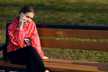 Child girl sitting on a bench and smiling while talking on the phoneの写真素材