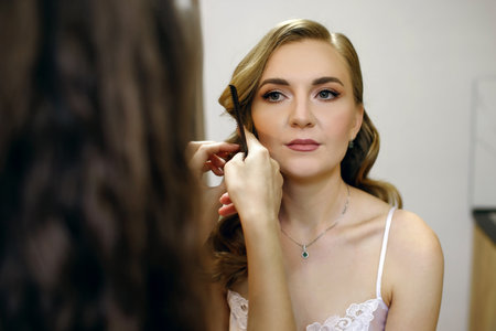 A hairdresser makes a beautiful hairstyle for a young woman at home on her wedding dayの写真素材