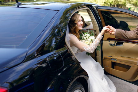 Groom helps happy young bride to get out of wedding car