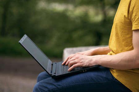 A man works in the street with a laptop. Remote work using modern technologies. Close-up view of hands and laptop. A freelance worker runs errands using a computer. Free space for textの写真素材