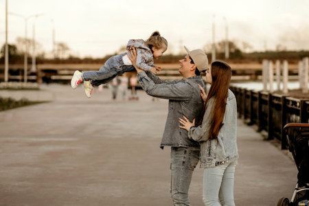 Happy stylish family in denim clothes walks along the river bank in the park. Dad, mom and daughter...