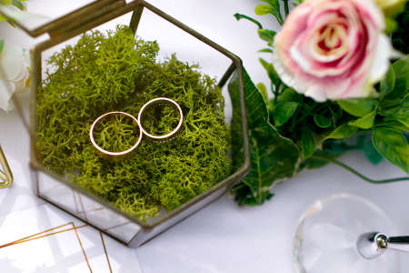 Gold wedding rings of the bride and groom lie in a glass box on the table for the wedding ceremony....
