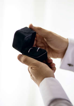 The groom is holding a black box with wedding rings. The groom's hands are holding wedding rings close-up in a vertical photoの写真素材