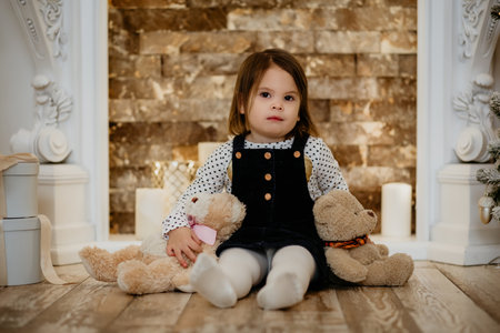 Portrait of a cute little girl with soft toys by the fireplace. Serious child girl enjoying New Year and Christmas winter holidays.の写真素材