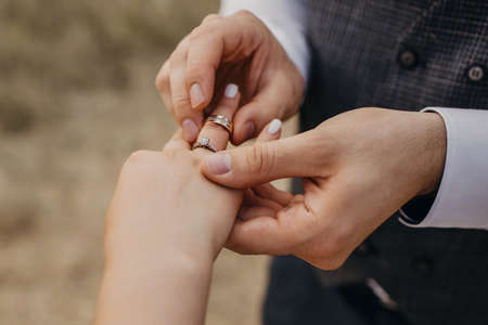 At the wedding ceremony, the groom puts the wedding ring on the bride's finger. Hands of newlyweds with rings close-up. Traditional wedding ceremony with rings donning and an oath of allegianceの写真素材