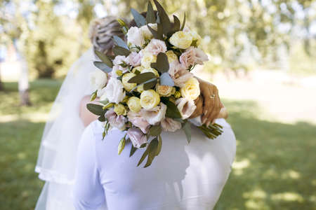 The lovely bride in a white dress hugs the groom and holds a beautiful bouquet of flowers in her hands. Wedding bouquet close-up of beautiful fresh flowersの写真素材