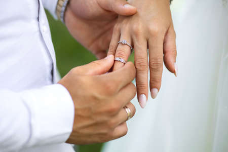 At the wedding ceremony, the groom puts a diamond engagement ring on the bride's finger, top view. Hands of newlyweds with rings close-up. Traditional wedding ceremony with putting on gold ringsの写真素材