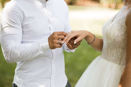 At the wedding ceremony, the groom puts the wedding ring on the bride's finger. Hands of newlyweds with rings close-up side view. Traditional wedding ceremony with putting on the ringsの写真素材