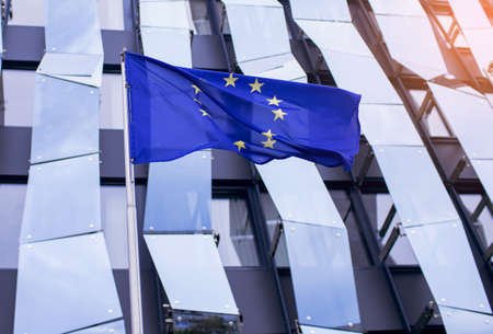 EU flag on the background of a glass office building with a geometric unusual design in blue. Symbol of European countries united in one democratic unionの写真素材