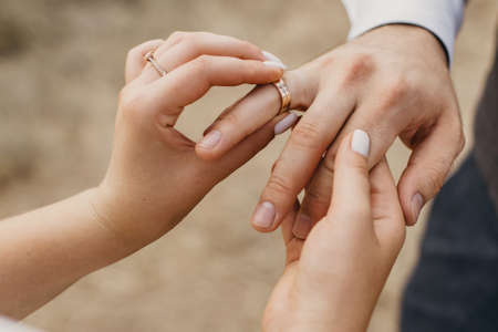 At the wedding ceremony, the bride puts the wedding ring on the groom's finger. Hands of newlyweds with wedding rings close-up. Heterosexual young couple in love at the moment of the wedding ceremonyの写真素材