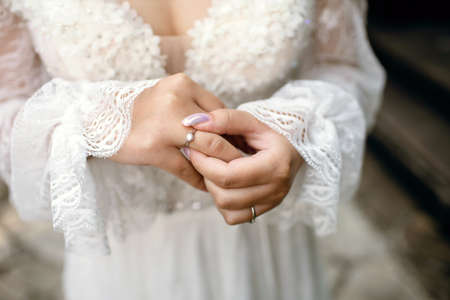 A bride in a white wedding dress and a beautiful manicure holds a gold wedding ring with a diamond with her fingers. Traditional wedding with exchange of rings between the bride and groomの写真素材