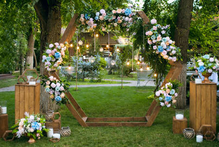 Wooden arch in the form of a regular hexagon for a wedding ceremony. The wedding arch is decorated with bright flowers and lights in the form of a garland. Beautiful wedding decorの写真素材