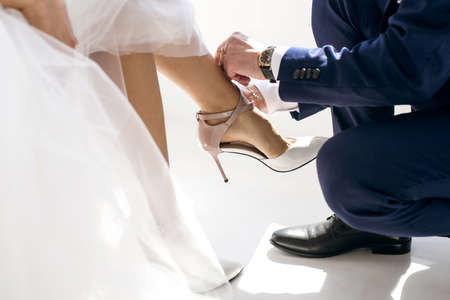 polite man helps a woman to put on her shoes. The groom takes care of his bride and on the wedding day neatly buttons up women's high-heeled shoes. Female shoes and male hands close upの写真素材
