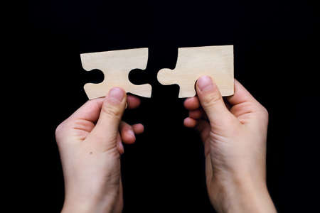 Two white wooden puzzles in the hands of a child on a black background close-up. Puzzle for the development of children's intelligence. Concept of connection and associationの写真素材