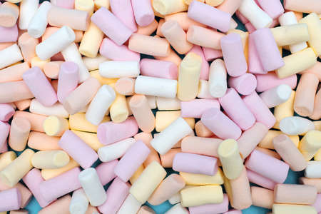 multi-colored marshmallows are scattered over a blue background. Delicious sweet dessert or...