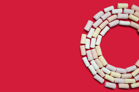 Multi-colored marshmallows are laid out in the form of a semicircle on a red background with free space for advertising or text. Marshmallow background as a decoration for a confectionery or coffeeの写真素材