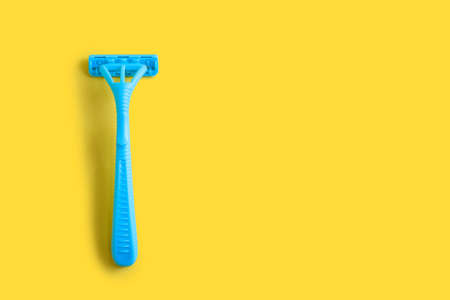 Disposable plastic razor on a yellow isolated background. Blue women's razor with free space for...
