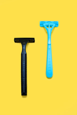 Two plastic razors in black and blue on a yellow background. Male and female disposable razor with free space for text. The concept of care for appearance and care for smooth skinの写真素材