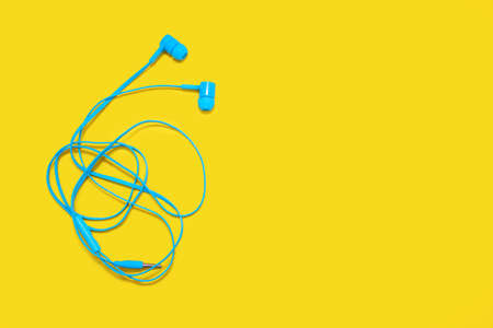 Tangled headphones lie on a yellow background. The blue headphones are twisted and it's a big problem to untangle them. Portable headphones with knots with space for textの写真素材