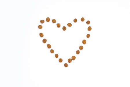 Dry pet food in the shape of a heart on a white isolated background. Healthy dry pet food in the center of the horizontal image. The concept of healthy food for animalsの写真素材