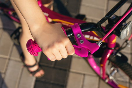 Handbrake on a pink children's bike close-up. The child's hand presses the handbrake. Bike safety concept. How to teach your child to ride a bike safelyの写真素材