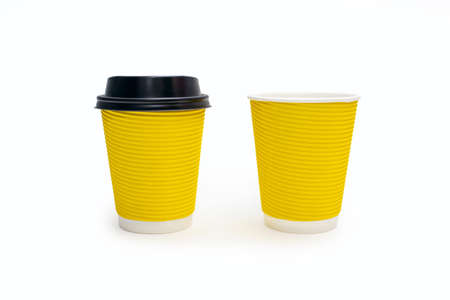 Two disposable yellow cardboard coffee cups on a white background. One coffee cup with plastic lid and one without. A variety of ways to drink coffee or tea from disposable cupsの写真素材