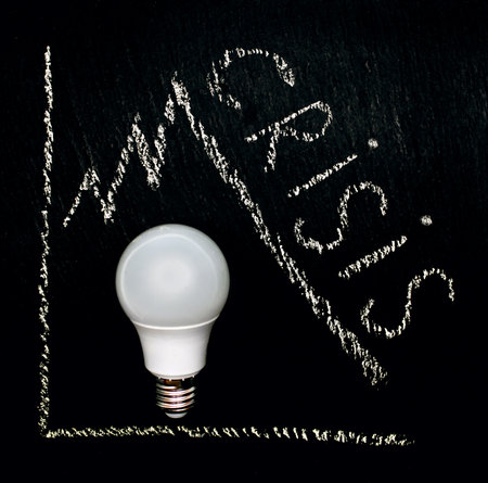 Chalk writing of the word crisis with a drawn diagram and a light bulb on a black rough background. Energy crisis and embargo on the sale of gas and oil in Europe. Lack of energy resourcesの写真素材