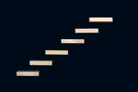 Wooden details lined up in the form of steps on a black background. Wooden rectangles form the shape of steps. The concept of career growth or rise from the bottom to the topの写真素材