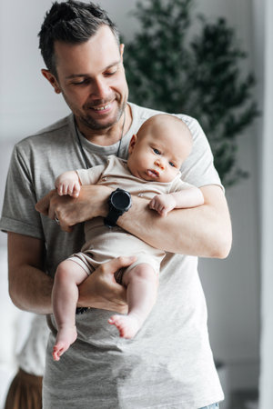 Loving dad holding his newborn baby and smiling. Stylish father and his cute newborn son. Parental relationship between father and son. Happy fatherhood and the joy of being a dadの写真素材