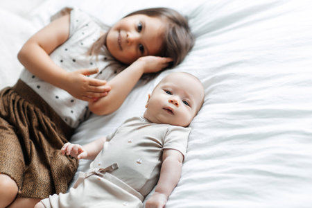 Little girl and her newborn brother are lying on the bed in the bedroom, top view. The children are resting on the bed. The children fall asleep in their bedroom. Free space for textの写真素材