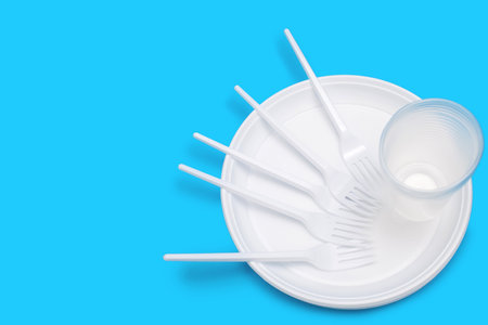 Disposable white plastic tableware in the form of plates, glasses and forks on a blue background. Plastic utensils for a picnic or outdoor party. Free space for textの写真素材