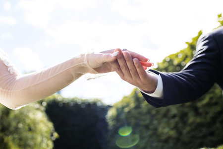 The bride and groom hold hands during the wedding ceremony against the backdrop of the sky. Hands of the bride and groom close-up. The groom gently took the bride by the handの写真素材