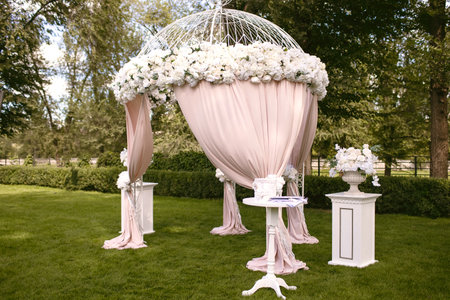 Beautiful wedding arch in the form of a tent on a green lawn, decorated with white flowers. Preparing for the wedding ceremony of the newlyweds. Wedding arch for ceremonies in the form of a tentの写真素材